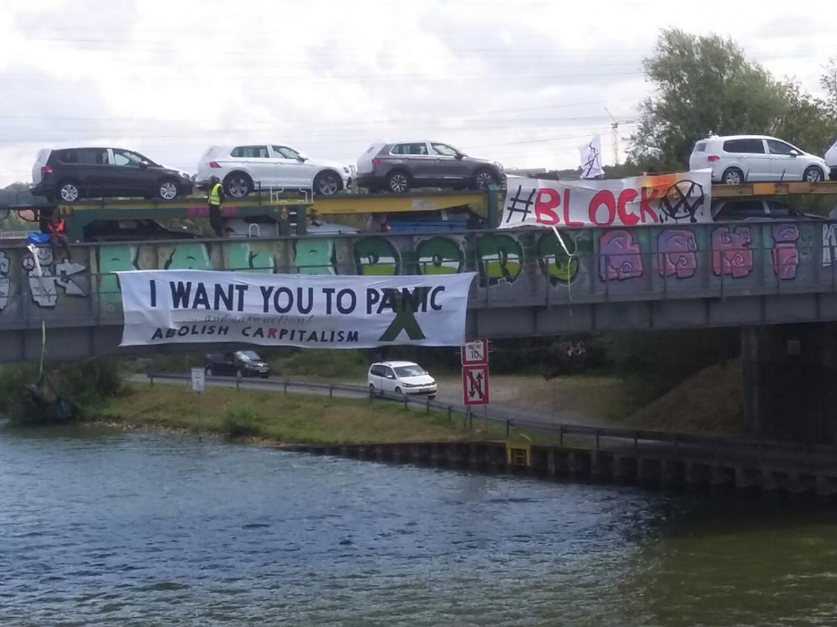 Aktivist*innen hängen von der Brücke herunter - auf einem Transpi zwischen ihnen steht "I want you to panic - abolish capitalism".