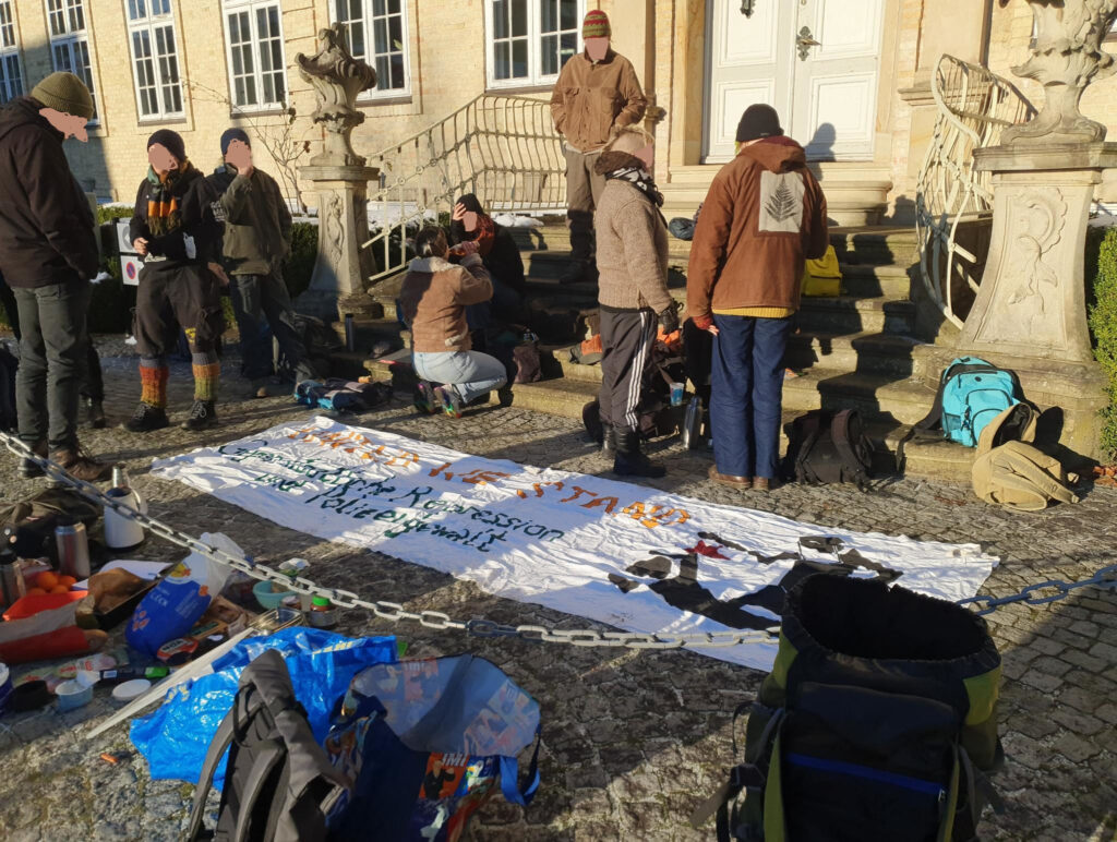Menschen picknicken vorm Gericht, dazwischen ein Transparent gegen Polizeigewalt und Repression